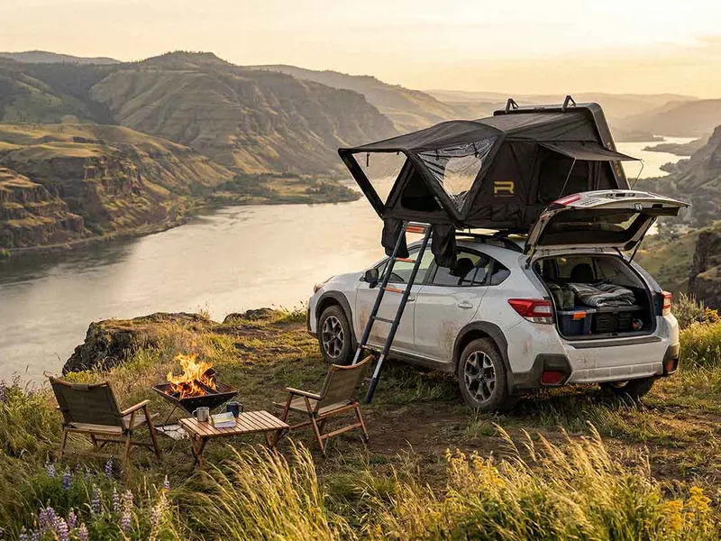 Roofnest Condor 2 Air hardshell rooftop tent open on a Subaru Crosstrek at a clifftop campsite with a campfire at sunset